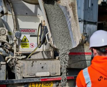 A man in orange PPE and a white hard hat watches low-carbon concrete being delivered for Holcim UK