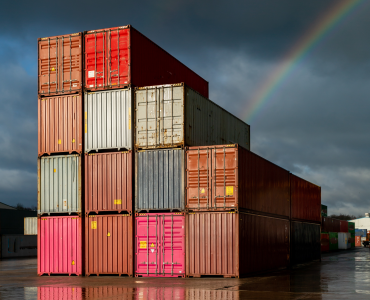 Multi-coloured containers stacked up in a yard with storm clouds and a rainbow in the background