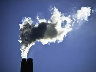 The top of a smoking industrial chimney with black and white smoke billowing from the top