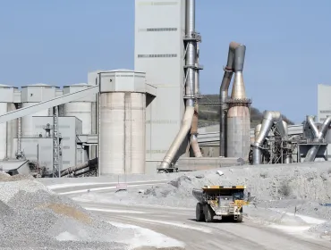 A yellow Caterpiller rigid dump truck (RDT) drives away from a huge cement factory 