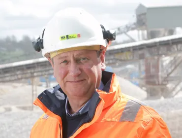 A head and shoulders picture of Mike Phillips, CEO of the British Aggregates Association, wearing orange PPE and a white hard hat, in a quarry.