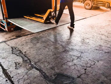 A man using a yellow trolly to unload a lorry onto a loading dock