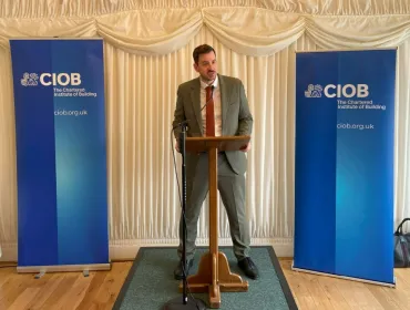 Mike Reader MP, the new chair of the All-Party Parliamentary Group for Excellence in the Built Environment, stands behind a podium, flanked by CIOB banners, speaking at the launch of the CIOB's Construction Client Guide: Leading Projects in the Built Environment, in Parliament last week.