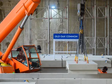 An orange crane and orange PPE-clad worker installing the first platforms at HS2's Old Oak Common station for HS2 trains.