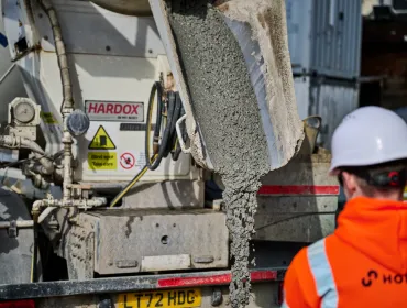 A man in orange PPE and a white hard hat watches low-carbon concrete being delivered for Holcim UK