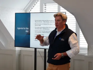 Mike Phillips, CEO British Aggregates Association, wearing a black, fleece gillet, open-necked white shirt and brown chinos, stands in front of a screen, speaking at the BAAs recent Landfill Tax consultation conference.