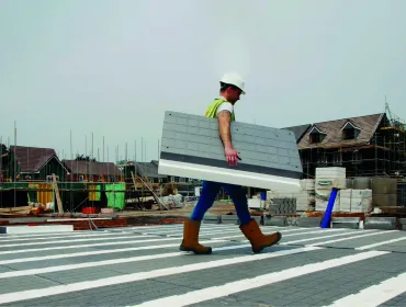A man in PPE walks across new floor made from Milbank Concrete Products' GDeck, while carrying a panel of the lightweight flooring system.