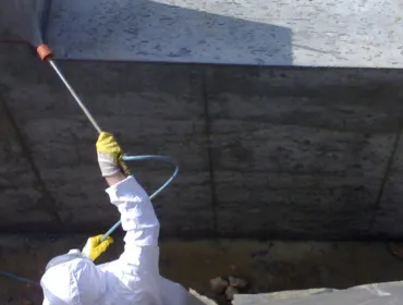 A man in white PPE Waterproofing underground sections of concrete with Vetrofluid using a low pressure pump.