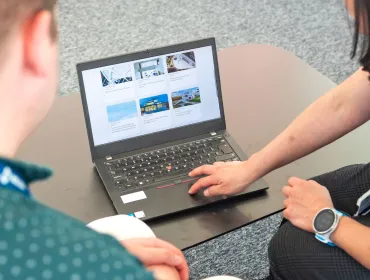Two people look at a laptop screen which shows several photos and text related to sustainable construction