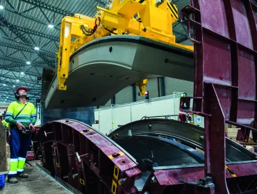 A yellow and blue PPE clad worker in a factory uses a mould and lifting device for precast tunnel segments, France, CBE