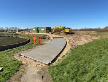 A waste water treatment plant with a CoMLaG mix access road in the foreground surrounded by grassy banks