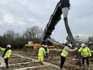 construction workers in yellow PPE lay concrete that's being delivered via chute from a concrete mixer