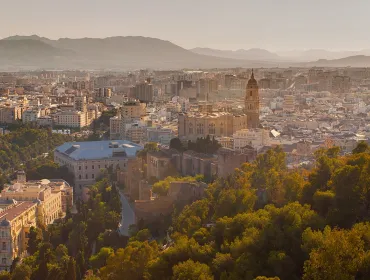 A panoramic photo of Malaga city centre with mountains in the distance, with the bullring lower right and a large church middle left.