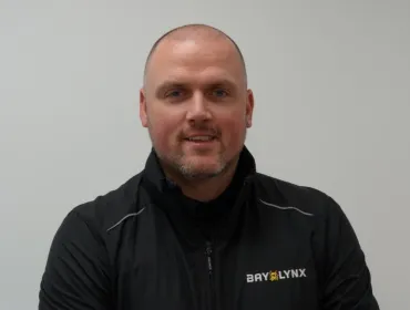 A bald man in a black fleece branded with the Bay-Lynx logo.