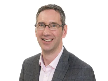 A head and shoulders shot of Peter Reekie of the Scottish Futures Trust will speak on sustainable infrastructure at the Glasgow Industry Day wearing glasses, an open necked pick shirt and a grey over-check jacket