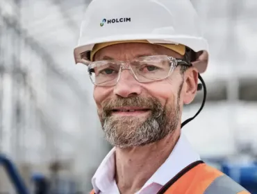 A head and shoulders photo of a man with a beard and glasses wearing PPE and a white hard hat