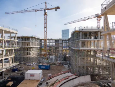 An under construction mid-rise building with two tower cranes in the background