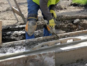 A construction worker using a trowel to help lay concrete foundations