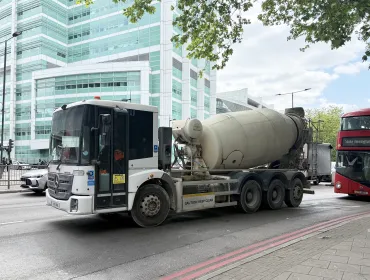 A concrete mixer drives along a street in London with a red double decker following 