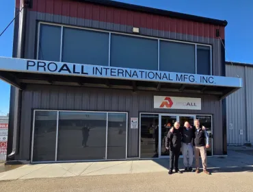Three men stand awith hands on each other's shoulders outside a two storey, ProAll branded building