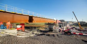 A steel bridge deck being slid into position with a crane in the background