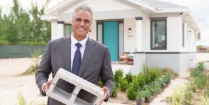 A man holding a concrete block outside a small house