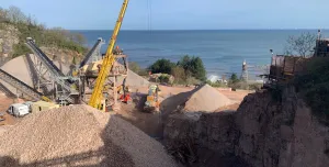 A picture of a yellow crane in a quarry with the sea in the background