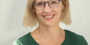 A head and shoulders picture of a blond haired woman in glasses and a green jumper