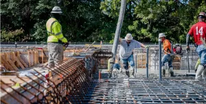 Four US construction workers in bright tshirts and PPE pour concrete