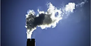 The top of a smoking industrial chimney with black and white smoke billowing from the top