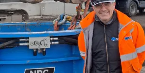 A man in orange PPE standing in front of a blue metal cylinder