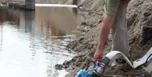 A man in red PPE holds a dewatering pump in water