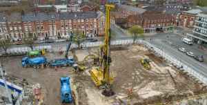 An aerial photo of a construction site with blue concrete mixers and concrete pump, and a yellow foundation rig