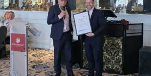 Two men in dark suits shake hands at an award ceremony
