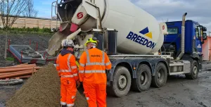 Two men in orange PPE in front of a concrete ready mix truck