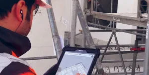 A man in orange PPE looking at a tablet screen