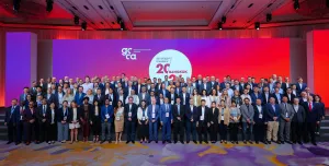 A large group of people standing infront of a white round sign and red lighting