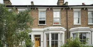 A man in shorts working in the front garden of a victorian terrace house