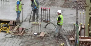 Three UK construction workers in PPE using a concrete pump to place concrete