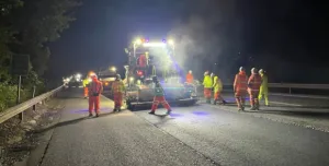 People in PPE repair a road at night