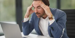 Stressed man working on a laptop in office. A businessman appears stressed and overworked in front of his laptop