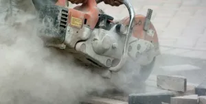 A close up of a hand-held concrete saw in use with silica dust clouds