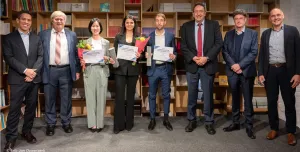 A line of people, some of whom are holding certificates,  standing in front of shelves celebrate winning the 2024 Förderpreis Beton Central Europe Competition