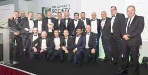 Lots of men in a line wearing black tie celebrate winning the Concrete Society’s annual Awards for Excellence in Concrete 2024 at The Royal Lancaster London
