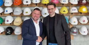 Christoph Miks (director customer solutions, core sensing), Michel Seeger (CEO, Vemaventuri) shake hands in front of a wall of multi-coloured construction hats