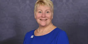 A head and shoulders photo of Caroline Gumble, CEO, Chartered Institute of Building (CIOB), wearing a blue dress, brooch and necklace.