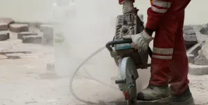 A man in red PPE using a hand-held concrete saw to repair a pavement