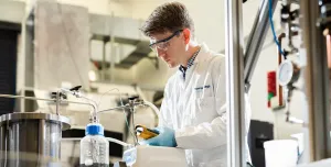 A man in lab coat and safety goggles working in a laboratory.
