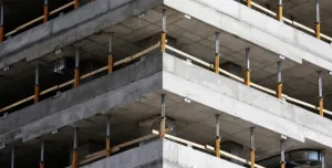 This image depicts a close-up view of a concrete multi-story building under construction, highlighting the raw structural elements such as concrete slabs and metal supports. The image conveys a sense of industrial progress and urban development in a modern city.