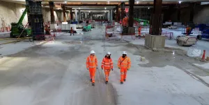 Three people in orange PPE walk across the competed base slab in the 850m long underground station box at Old Oak Common.